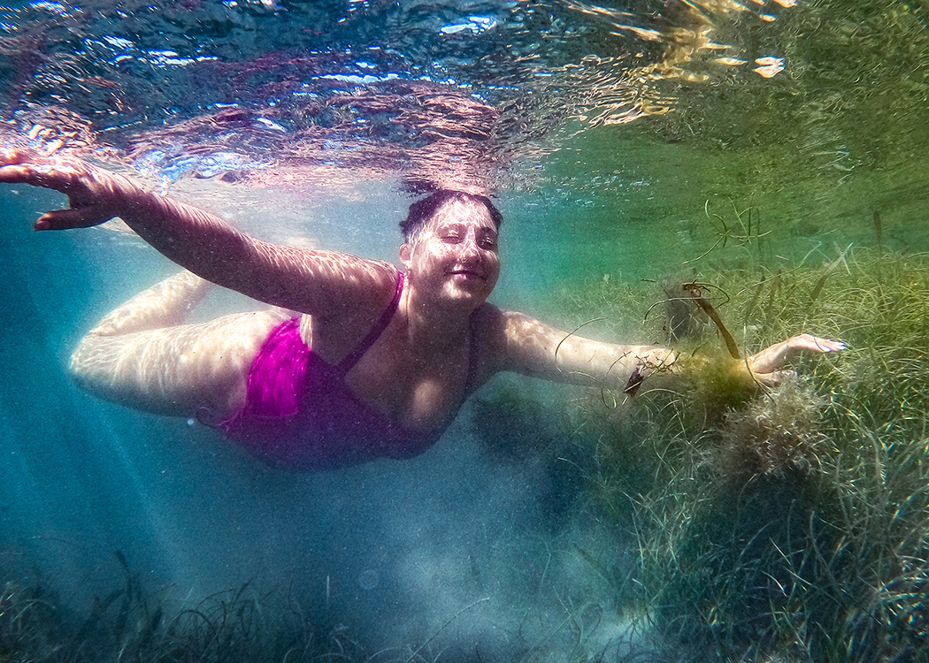 woman smiling swimming underwater holding seaweed