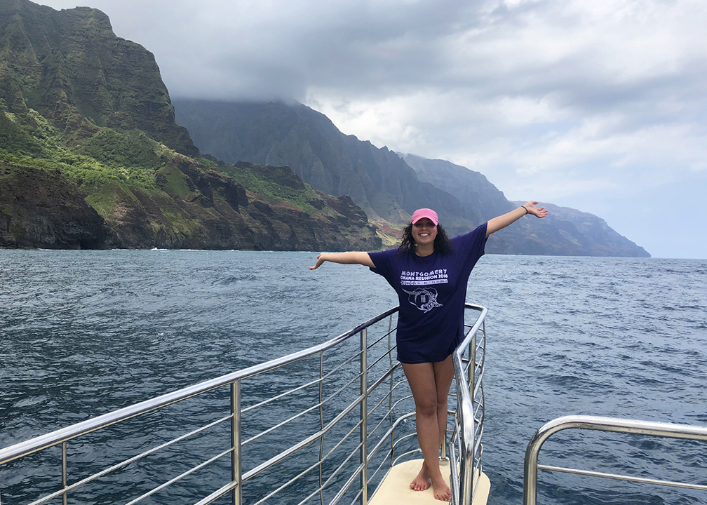 woman smiling standing on boat by Kauai mountain ridges