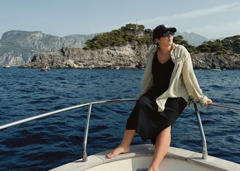 woman sitting on boat in blue sea by Amalfi Coast