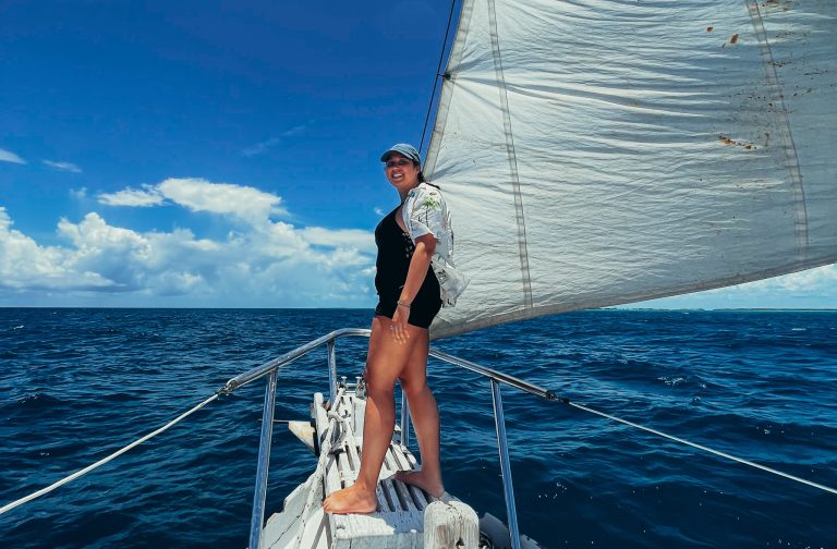 woman standing on sail boat edge facing blue sea