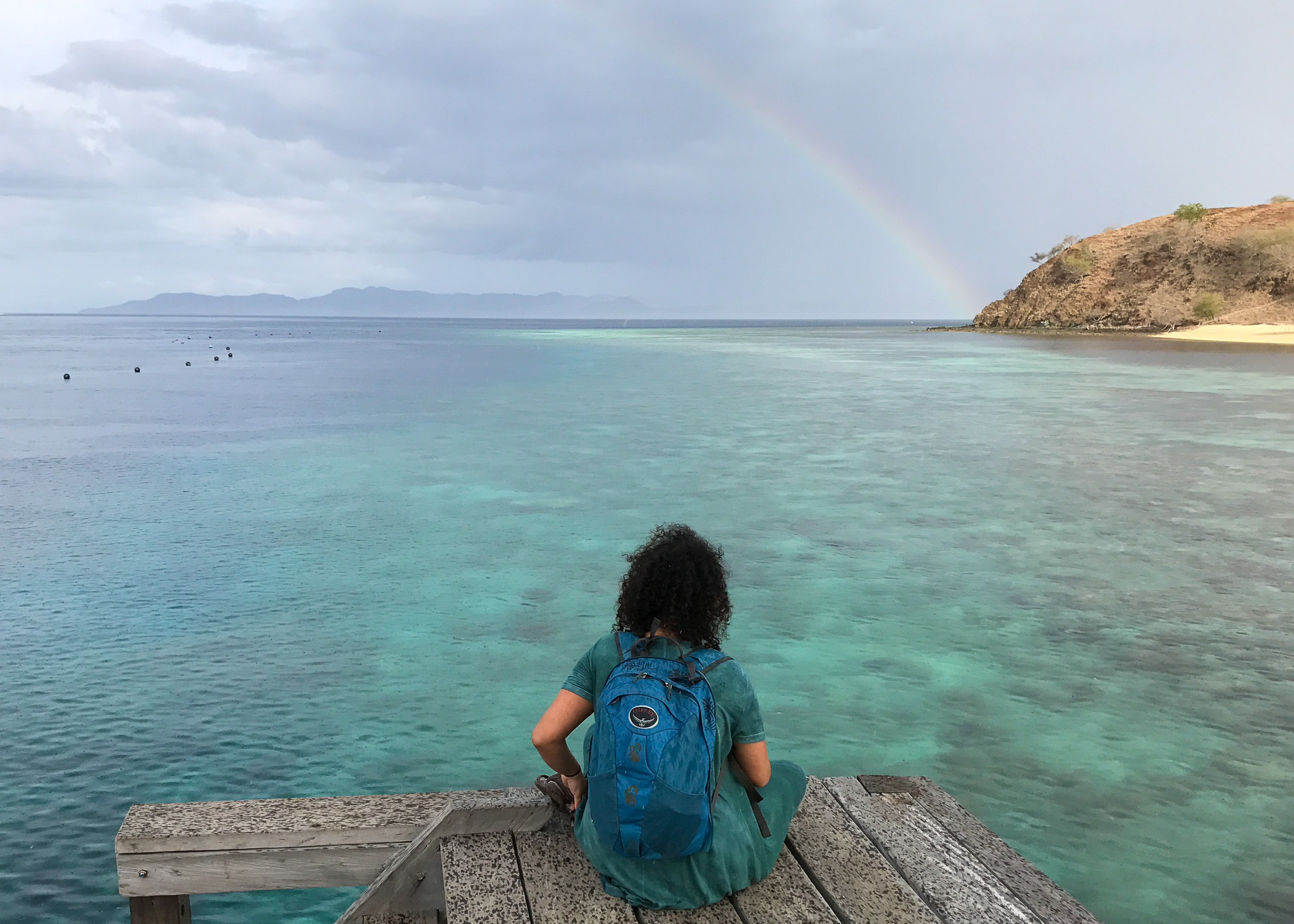 woman sitting by turquoise sea and rainbow