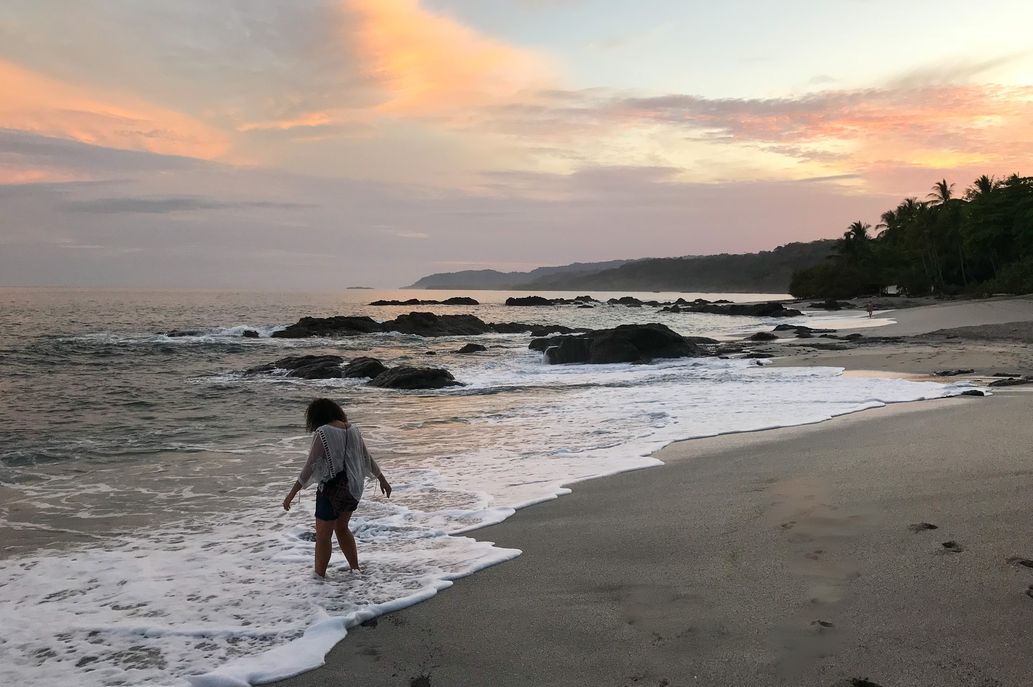 woman in beach waves under pink sky sunset